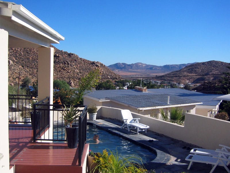 Terrasse und kleiner Pool eines Gästehauses am Hang, dahinter Dächer von Springbok und kahle Granitberge