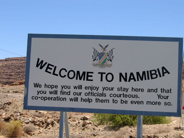 Schild „Welcome to Namibia“ mit dem namibischen Staatswappen vor einem steinigen Hang