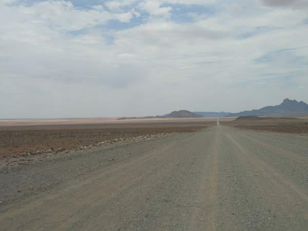 Gerade Schotterstraße unter grauem Himmel, am Horizont Berge