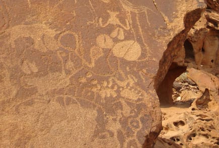 Engraved animal figures and circles on a reddish sandstone slab, with a weathered rock hollow on the right