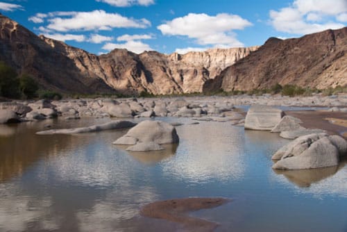 Smooth pale boulders in the shallow river with steep canyon walls behind