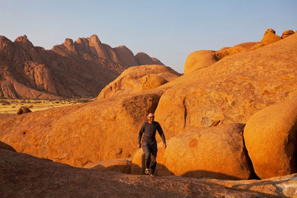 Hiker among rounded red granite boulders, the Spitzkoppe peaks behind