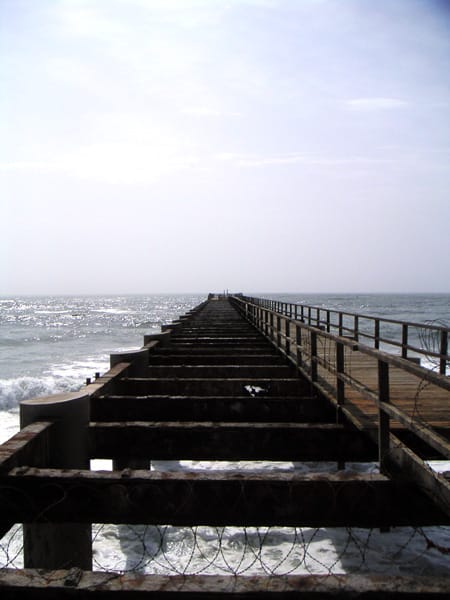 Iron pier with missing planks and barbed wire, the sea beyond