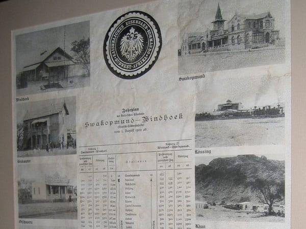Gerahmter Fahrplan der Bahn Swakopmund nach Windhoek von 1902 mit Reichsadler-Siegel und alten Bahnhofsfotos
