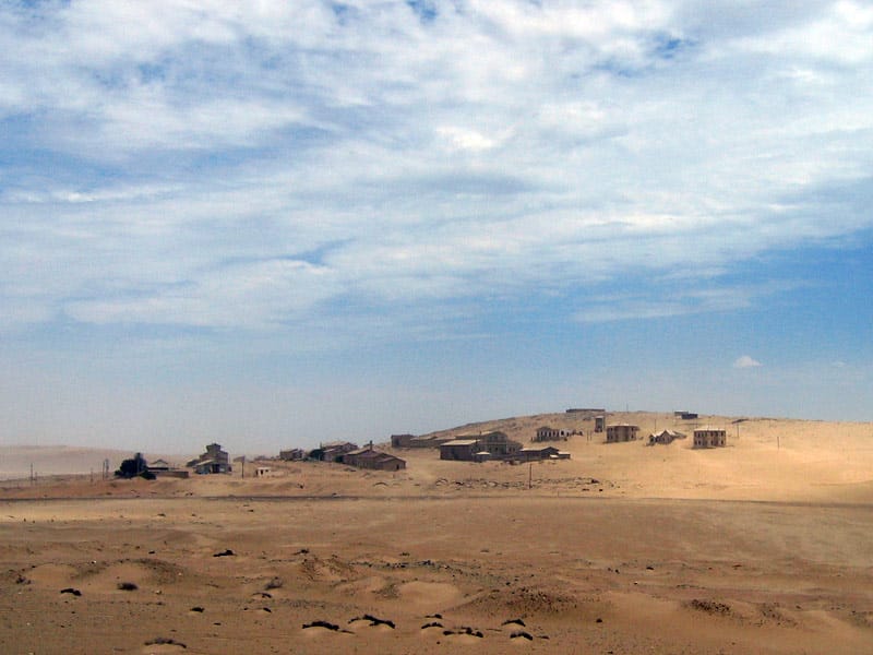 Verstreute Steinhäuser auf einem flachen Sandhügel unter leicht bewölktem Himmel