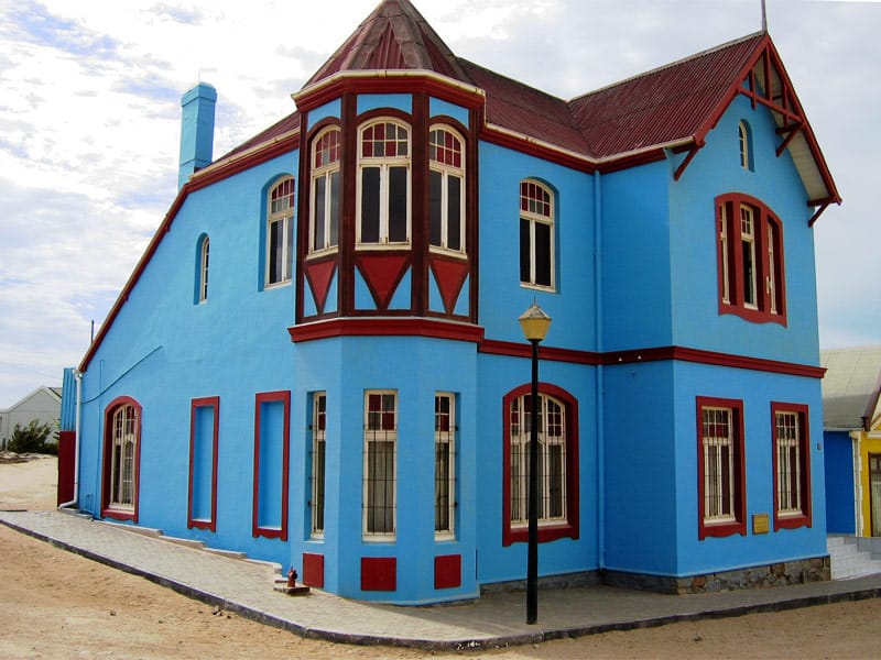 Bright blue house with red window frames and a bay window on a street corner