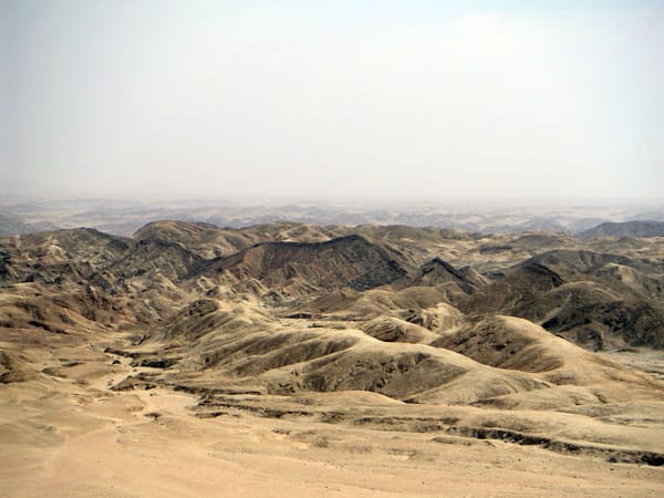 Bare, folded hills in grey and beige stretching to a hazy horizon