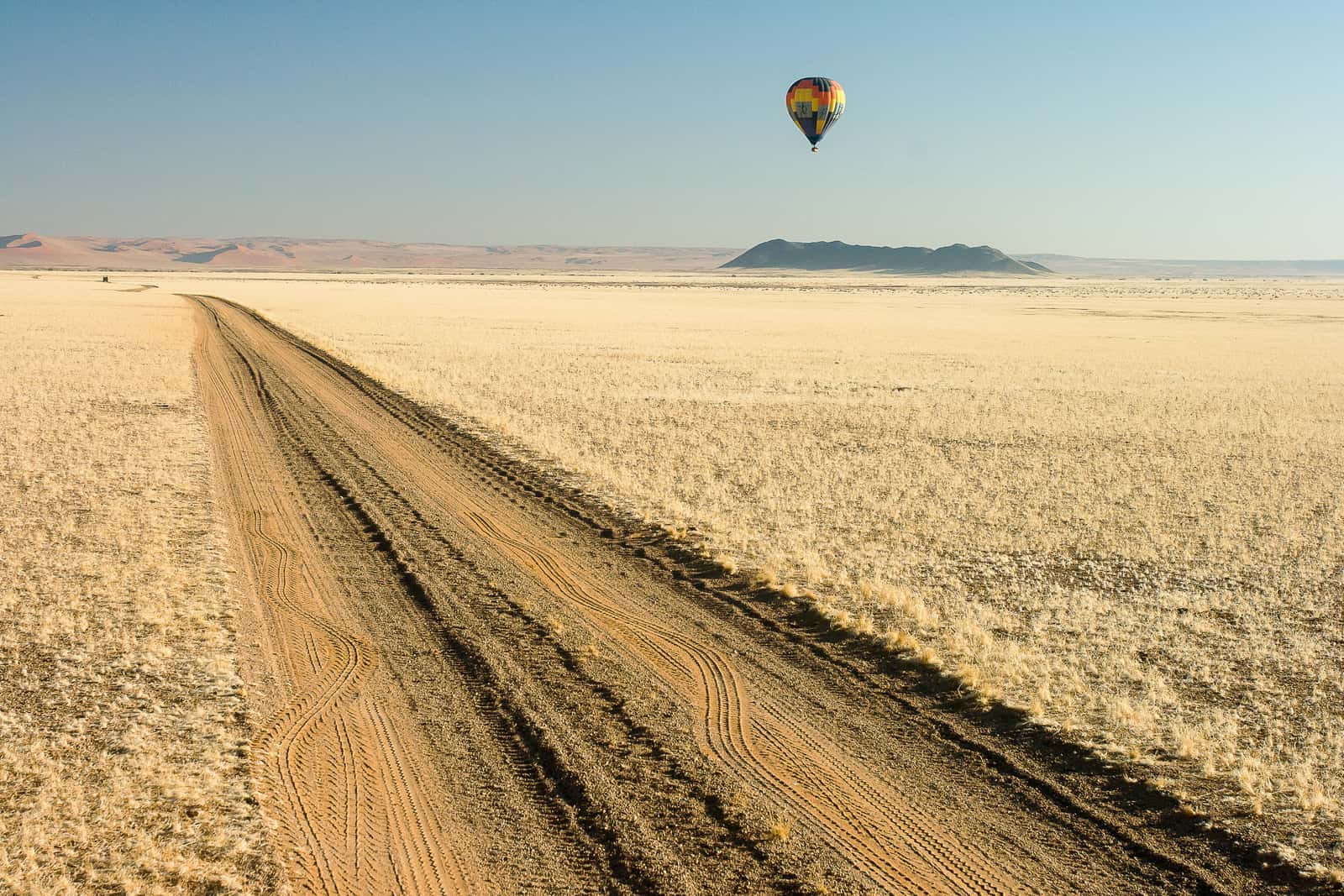 Straight gravel road running to the horizon, a hot-air balloon above it