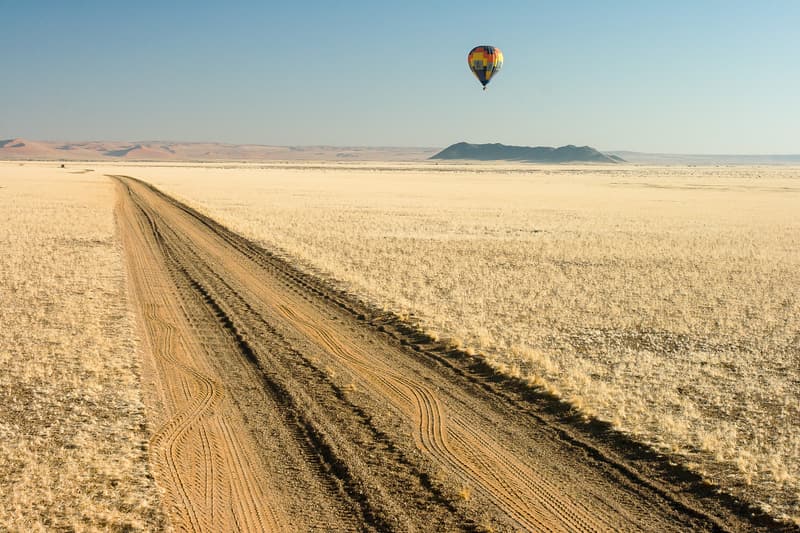 Gerade Schotterpiste bis zum Horizont, darüber ein Heißluftballon