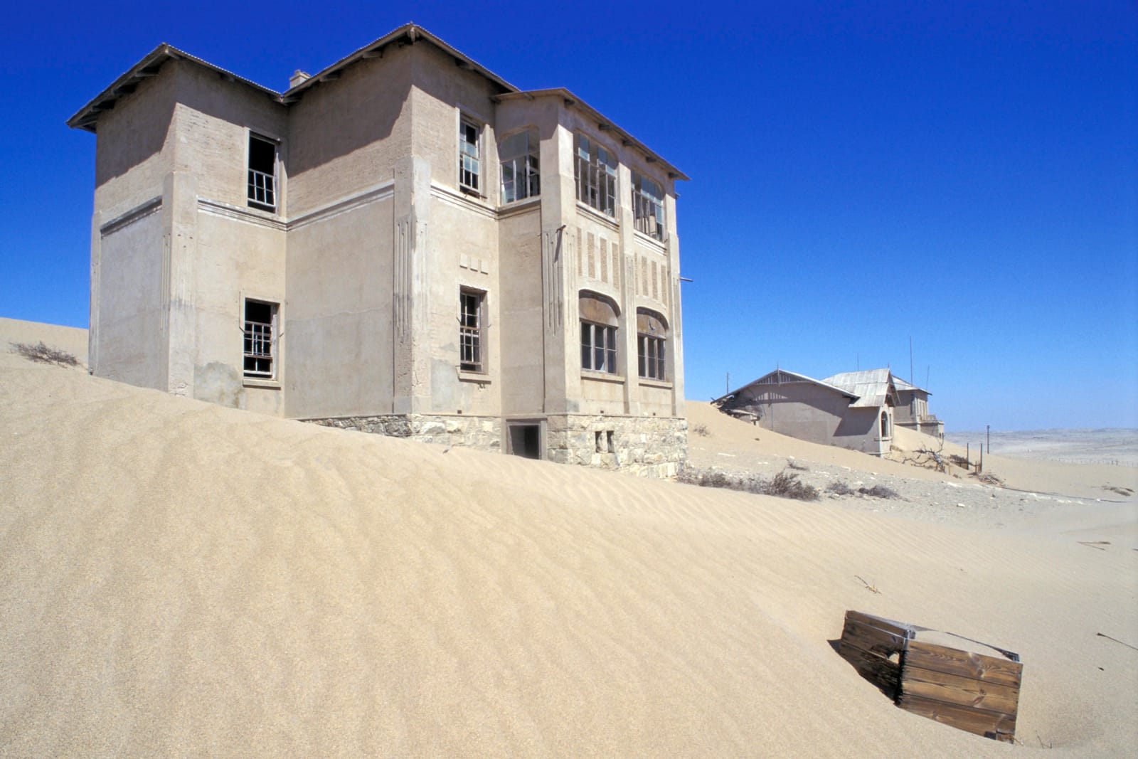 Verlassenes zweistöckiges Haus in Kolmanskop, davor eine Sanddüne